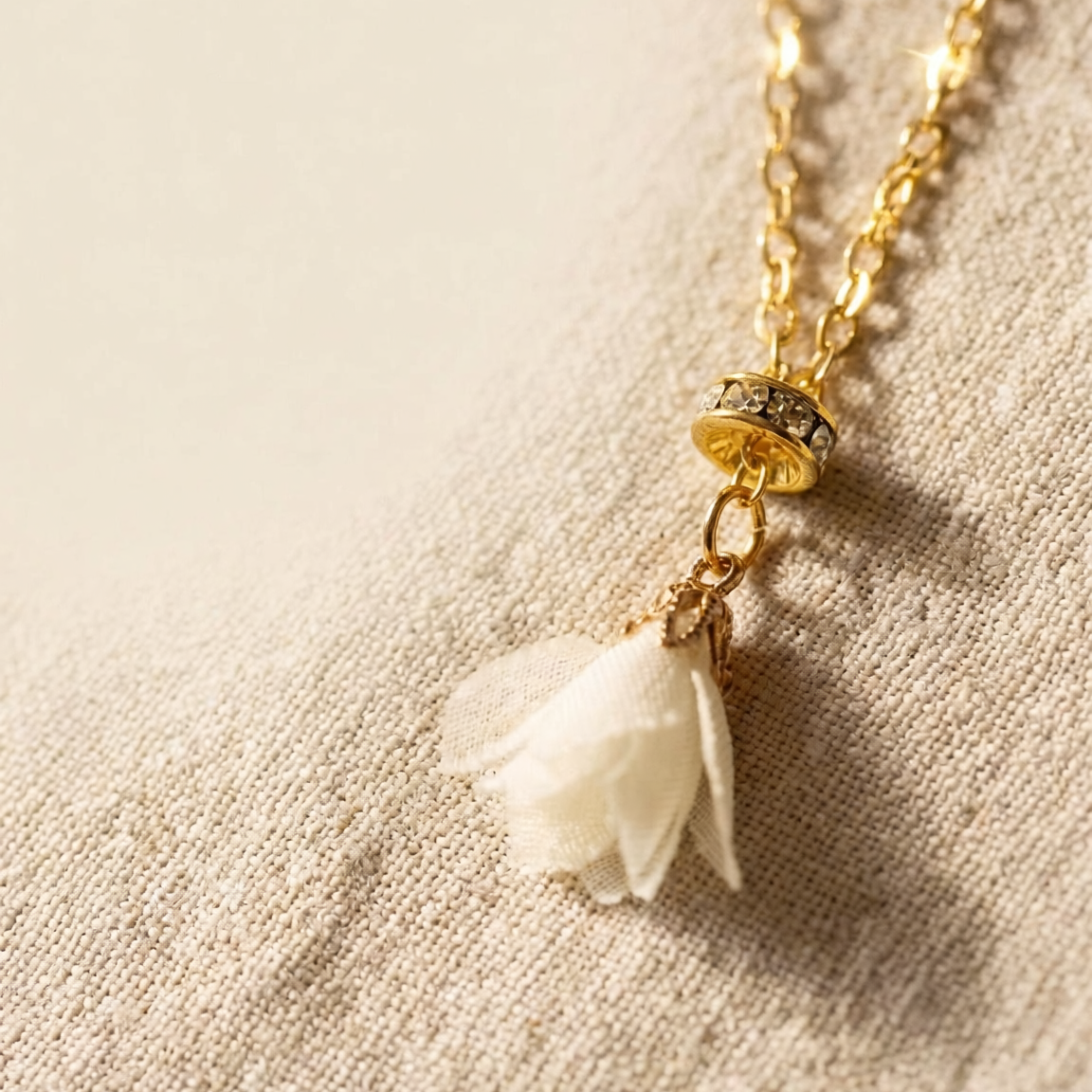 Gold necklace with a white flower pendant on a beige fabric background