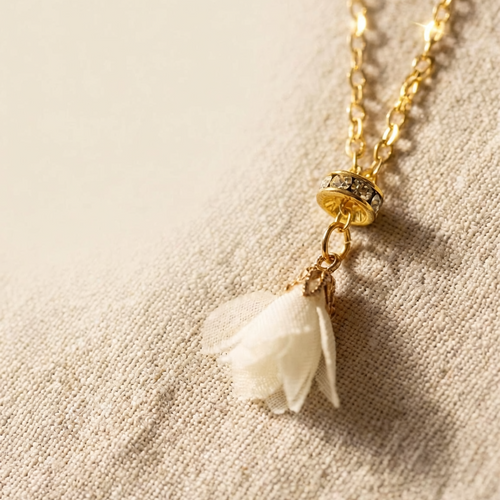 Gold necklace with a white flower pendant on a beige fabric background
